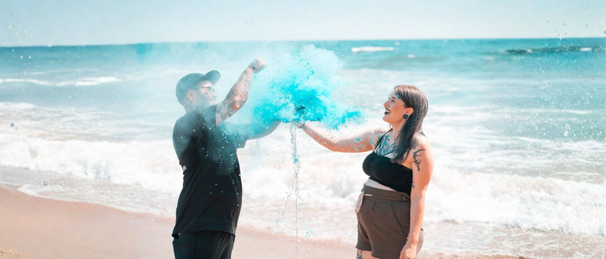 A man and a woman on a beach with the ocean in the background, creating a large burst of bright blue powder in the air.